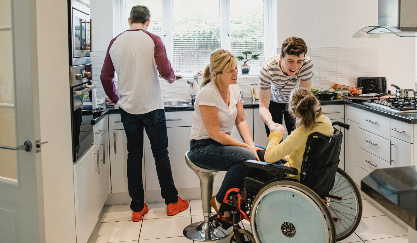 A mom, dad, brother and sister who is in a wheelchair in a kitchen setting