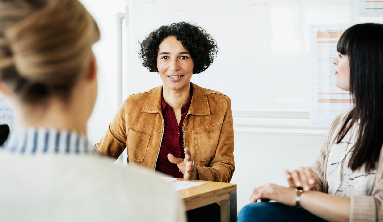 Middle aged woman in a conference room setting speaking with two other women.