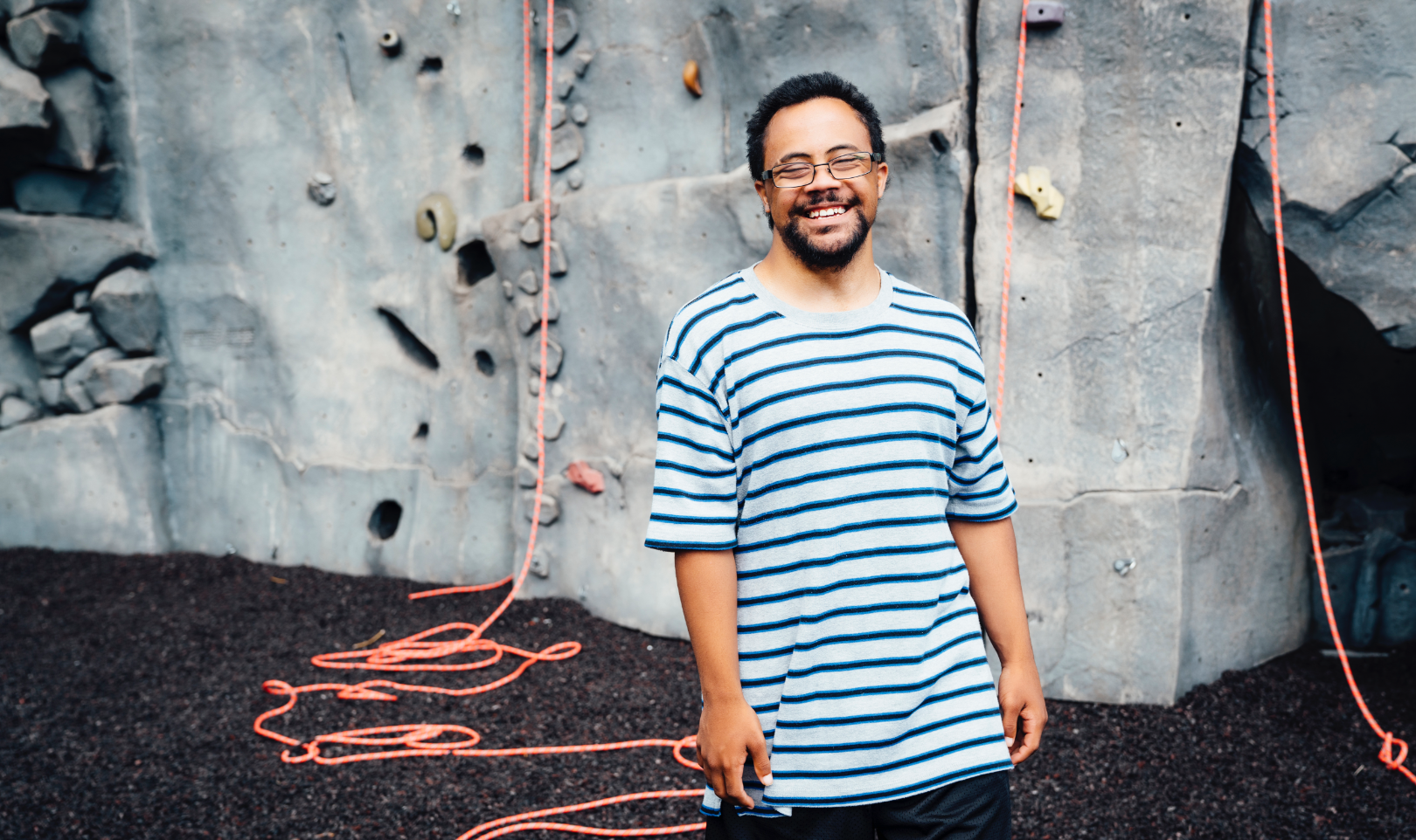 Man standing infront of rock climbing wall smiling